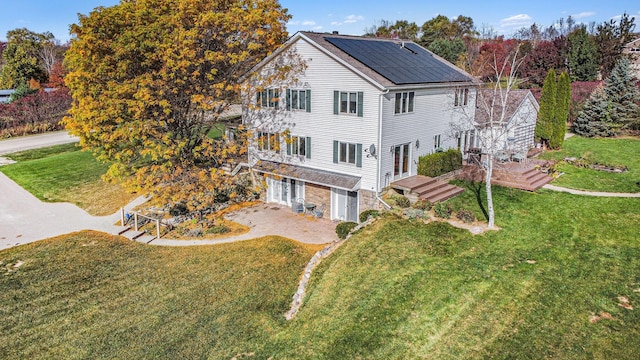 exterior space featuring driveway, an attached garage, solar panels, and a front yard