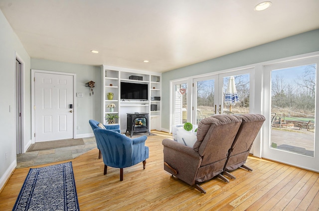 living room featuring a wood stove, recessed lighting, baseboards, and light wood finished floors