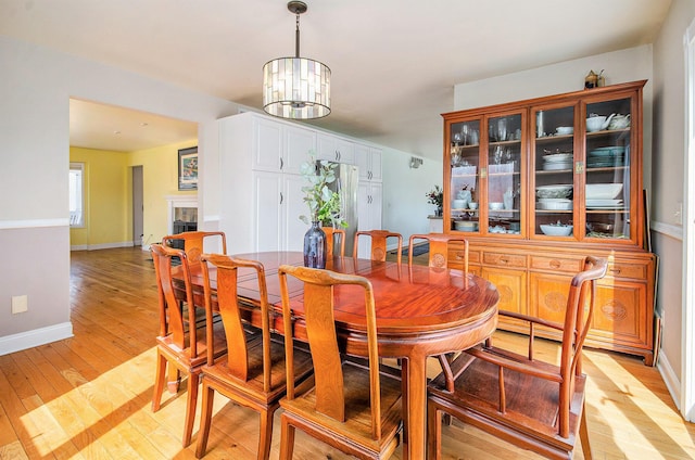 dining area with baseboards, a notable chandelier, light wood-style flooring, and a tile fireplace