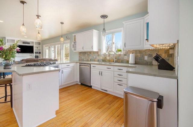 kitchen with a wealth of natural light, light wood-style flooring, appliances with stainless steel finishes, a peninsula, and a sink