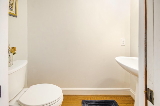 half bathroom with baseboards, toilet, and wood finished floors