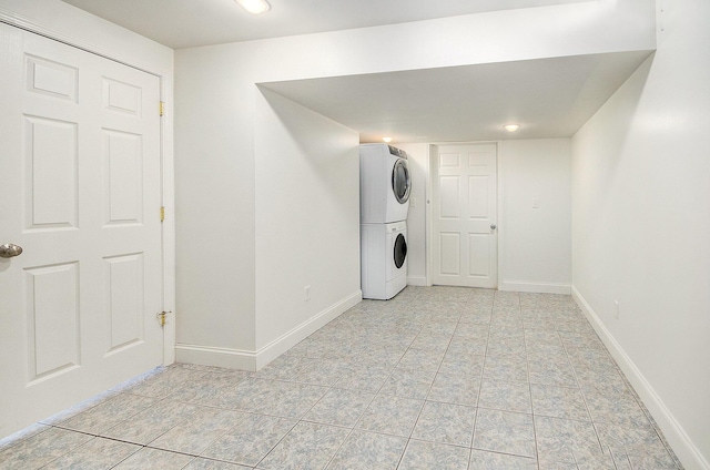 washroom featuring light tile patterned floors, stacked washer / drying machine, baseboards, and laundry area