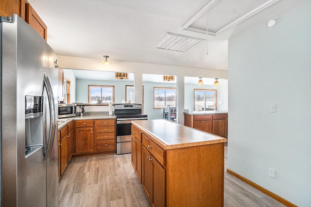 kitchen with light countertops, stainless steel appliances, a kitchen island, light wood-style floors, and brown cabinetry