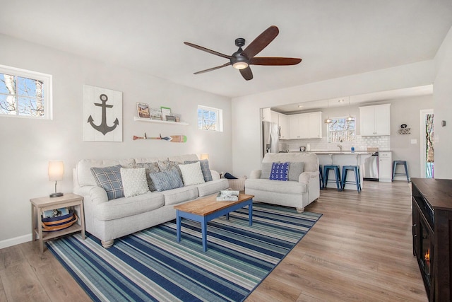 living room featuring light wood-type flooring, baseboards, and ceiling fan