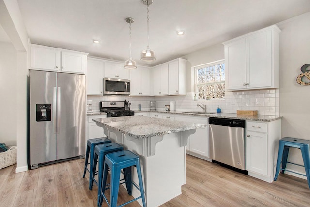 kitchen with a kitchen island, a sink, white cabinets, appliances with stainless steel finishes, and light wood-type flooring