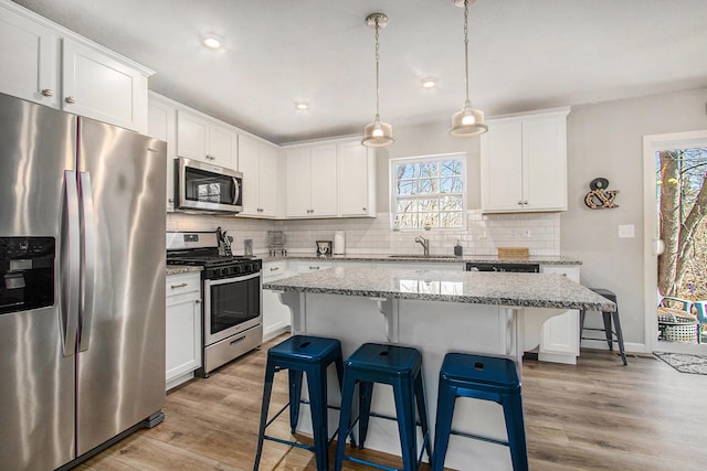 kitchen with a sink, white cabinets, light wood-style floors, appliances with stainless steel finishes, and a kitchen breakfast bar