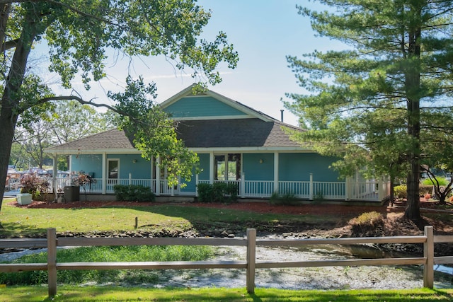 farmhouse featuring roof with shingles, covered porch, a front yard, and fence