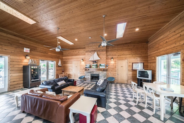 living area featuring plenty of natural light, a stone fireplace, a skylight, wood ceiling, and a towering ceiling