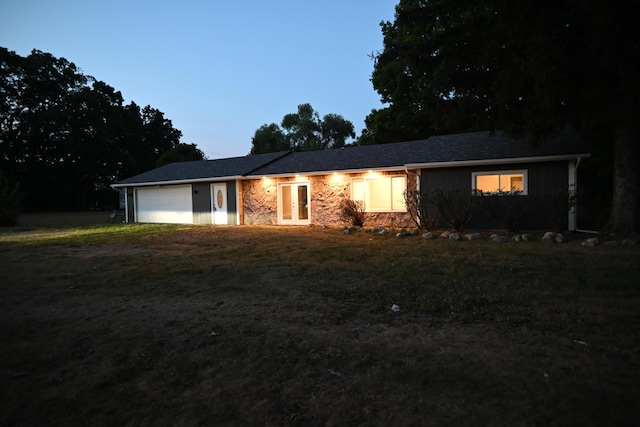 ranch-style house featuring an attached garage, a front yard, french doors, stone siding, and driveway