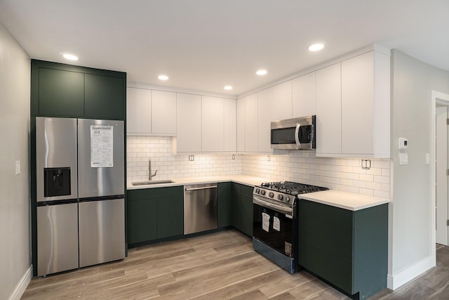 kitchen featuring light wood-style flooring, a sink, appliances with stainless steel finishes, light countertops, and decorative backsplash