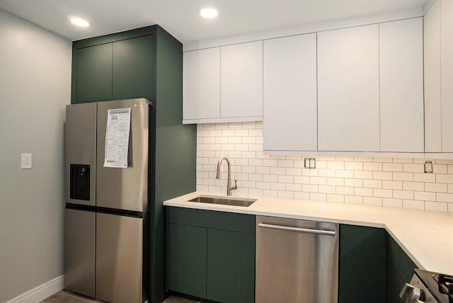 kitchen with a sink, tasteful backsplash, stainless steel appliances, light countertops, and green cabinetry