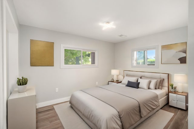 bedroom with baseboards, multiple windows, visible vents, and wood finished floors