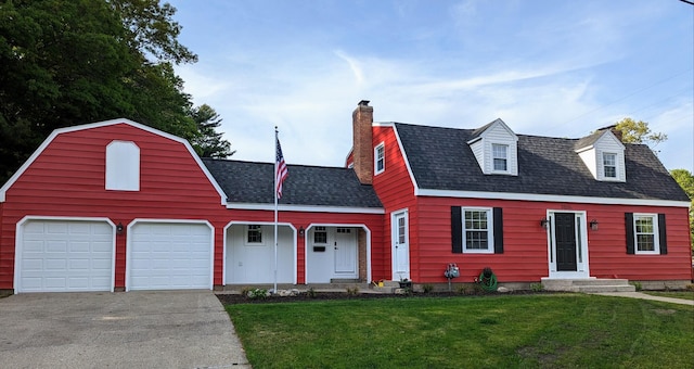 view of front of property featuring a gambrel roof, concrete driveway, a front yard, a shingled roof, and a chimney