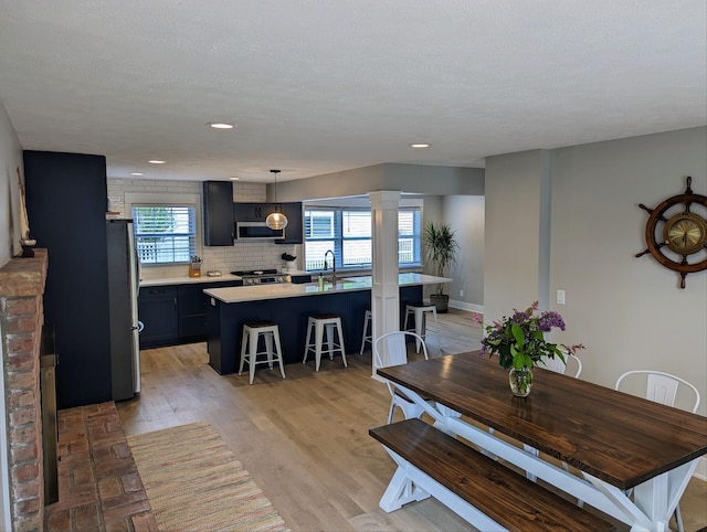 dining room with baseboards, light wood-style flooring, decorative columns, recessed lighting, and a textured ceiling