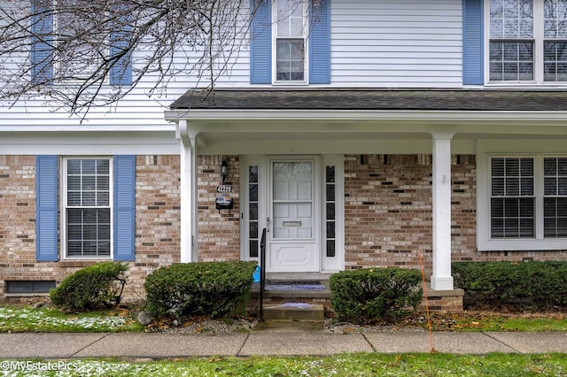 view of exterior entry with brick siding and roof with shingles