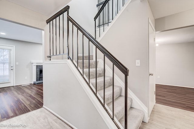 stairway featuring a brick fireplace, wood finished floors, and baseboards