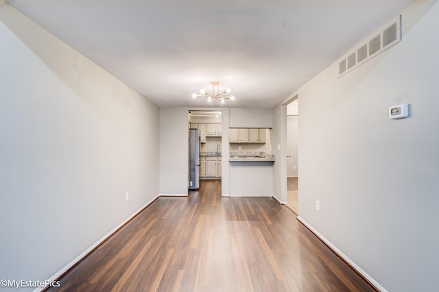 unfurnished living room with visible vents, a sink, baseboards, a chandelier, and dark wood-style flooring