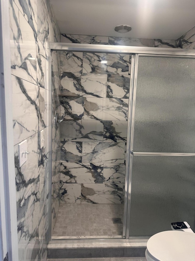 full bathroom with a marble finish shower and toilet