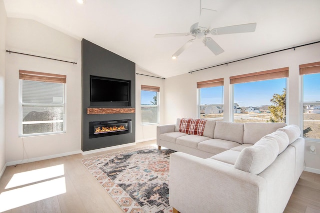 living room with lofted ceiling, light wood-style flooring, a healthy amount of sunlight, and a large fireplace