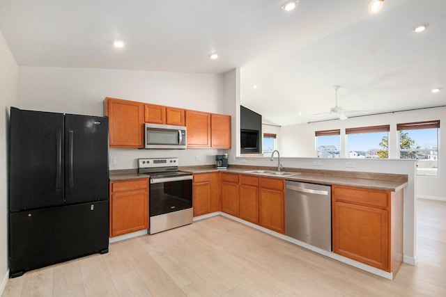 kitchen with a peninsula, lofted ceiling, a sink, stainless steel appliances, and light wood-style floors