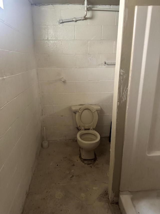 bathroom with unfinished concrete flooring, toilet, and concrete block wall