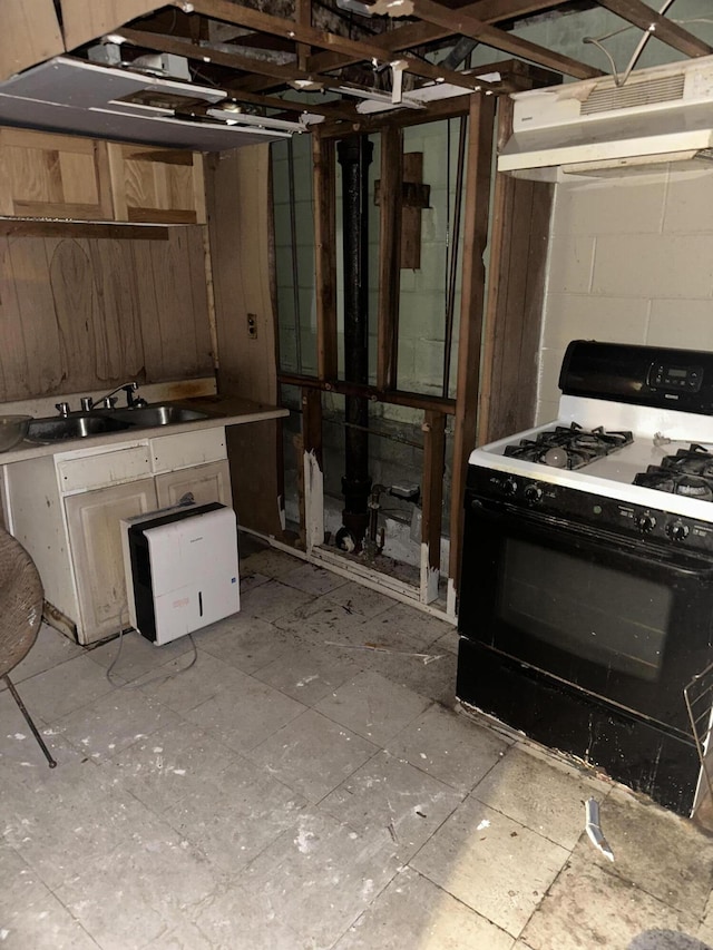 kitchen featuring gas stove, under cabinet range hood, concrete block wall, and a sink