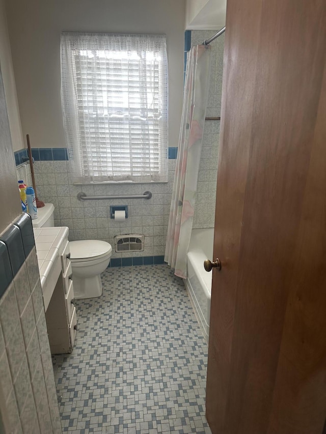 full bath featuring vanity, shower / tub combo, wainscoting, tile walls, and toilet