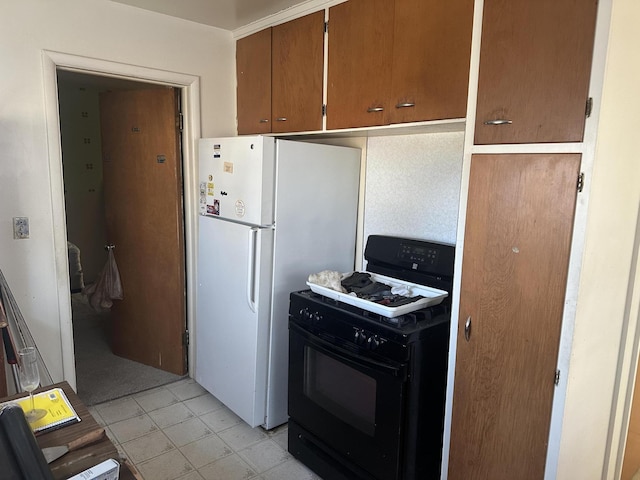 kitchen with light tile patterned floors, brown cabinetry, gas stove, and freestanding refrigerator