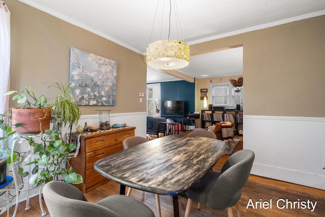 dining space featuring crown molding, wood finished floors, and a wainscoted wall