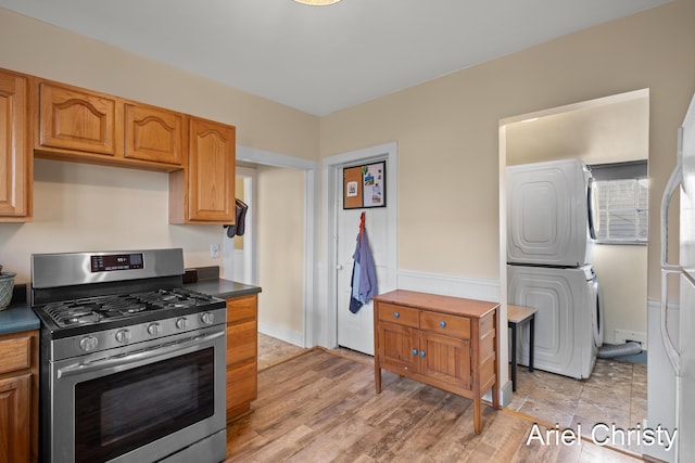 kitchen with dark countertops, stacked washer and dryer, stainless steel range with gas stovetop, and light wood-type flooring