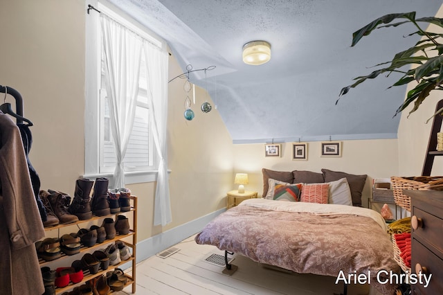 bedroom featuring visible vents, baseboards, lofted ceiling, wood finished floors, and a textured ceiling