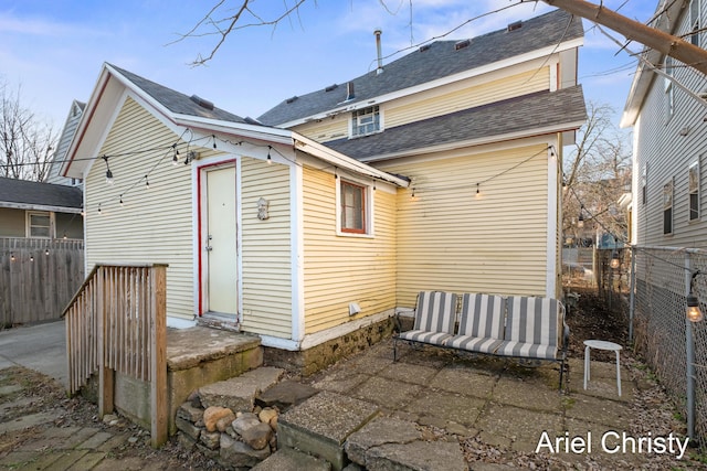 back of property with a patio, a shingled roof, and fence