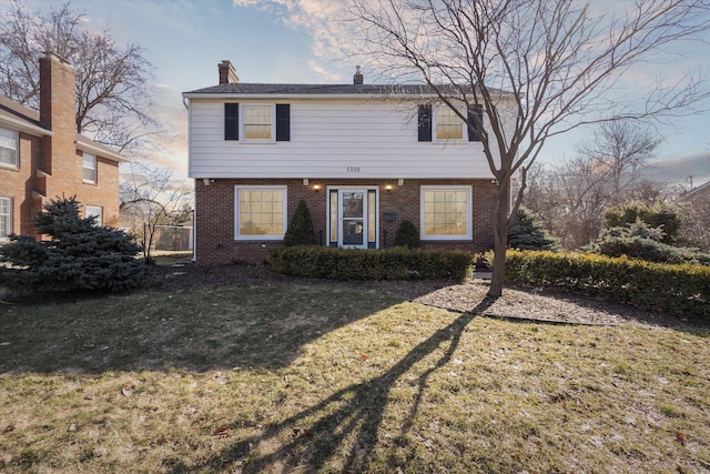 colonial home featuring brick siding, a chimney, and a front yard