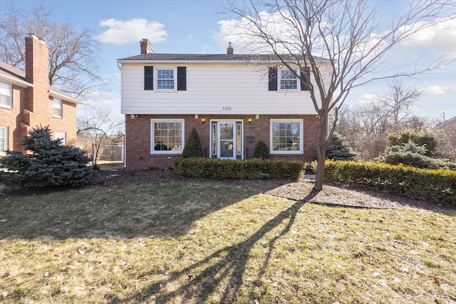 colonial house featuring brick siding, a chimney, and a front lawn