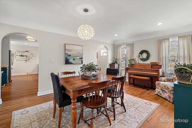 dining area featuring light wood-style flooring, visible vents, arched walkways, and a wealth of natural light