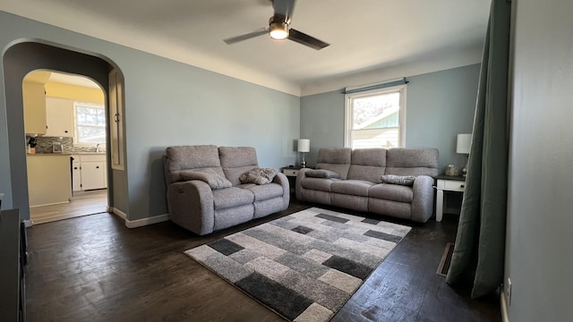 living area with a ceiling fan, arched walkways, dark wood-style flooring, and baseboards