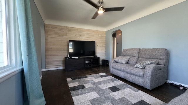 living area with dark wood finished floors, arched walkways, wood walls, ceiling fan, and an accent wall