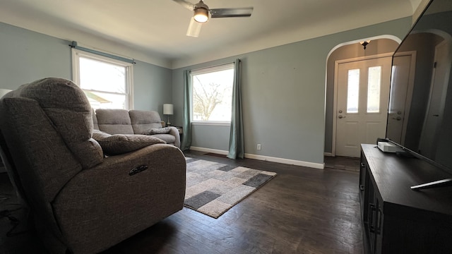 living area with baseboards, arched walkways, dark wood finished floors, and a ceiling fan