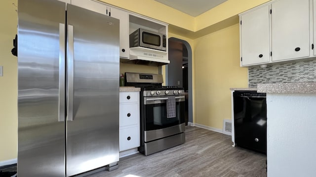 kitchen featuring light wood-type flooring, decorative backsplash, arched walkways, white cabinets, and stainless steel appliances