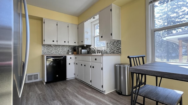 kitchen with visible vents, black dishwasher, dark wood finished floors, stainless steel fridge, and decorative backsplash