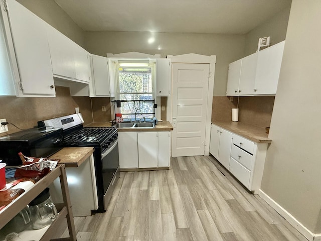 kitchen with gas stove, baseboards, light wood-style flooring, a sink, and white cabinetry