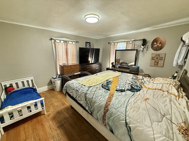 bedroom featuring ornamental molding, a textured ceiling, baseboards, and wood-type flooring