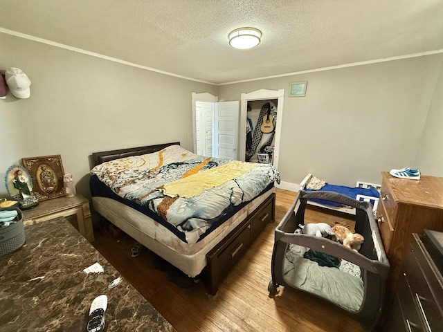 bedroom featuring ornamental molding, a textured ceiling, baseboards, and wood finished floors