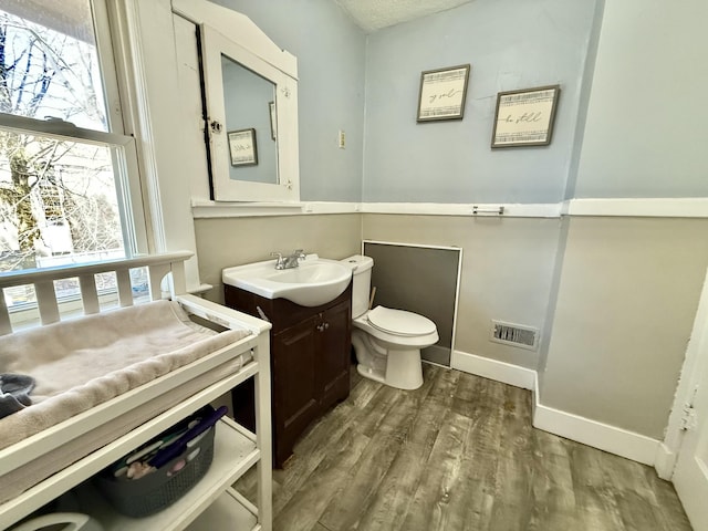 half bathroom featuring visible vents, baseboards, toilet, wood finished floors, and vanity