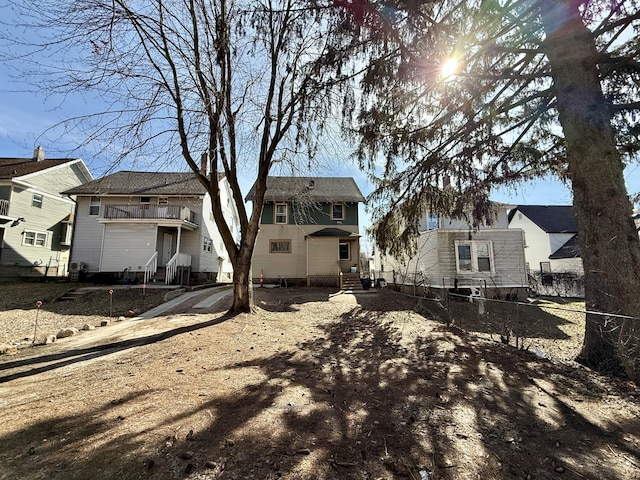 rear view of house with entry steps, a balcony, fence, and a residential view