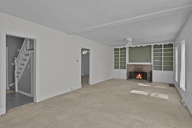 unfurnished living room with a fireplace with flush hearth, stairs, carpet, and ceiling fan