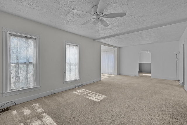 empty room featuring visible vents, a ceiling fan, arched walkways, carpet floors, and baseboards