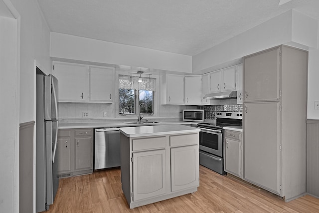 kitchen featuring a sink, under cabinet range hood, stainless steel appliances, light wood-style floors, and light countertops