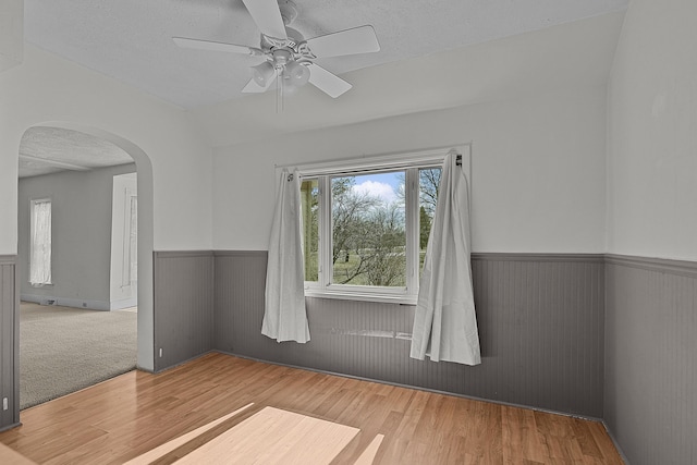 spare room with a ceiling fan, a textured ceiling, wood finished floors, arched walkways, and wainscoting