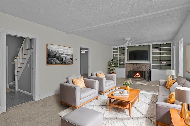 carpeted living area featuring a textured ceiling, stairway, a lit fireplace, and ceiling fan